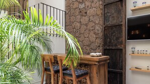 A wooden table and chairs in a stone-walled courtyard with a staircase and shelves with glasses.