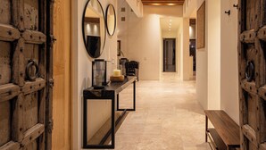 A hallway with wooden beams on the ceiling, a bench, and two doors with intricate designs.