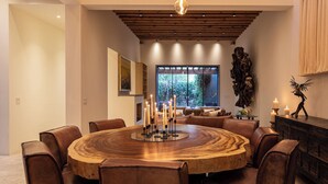 A modern dining area with a wooden round table, leather chairs, and hanging pendant lights.