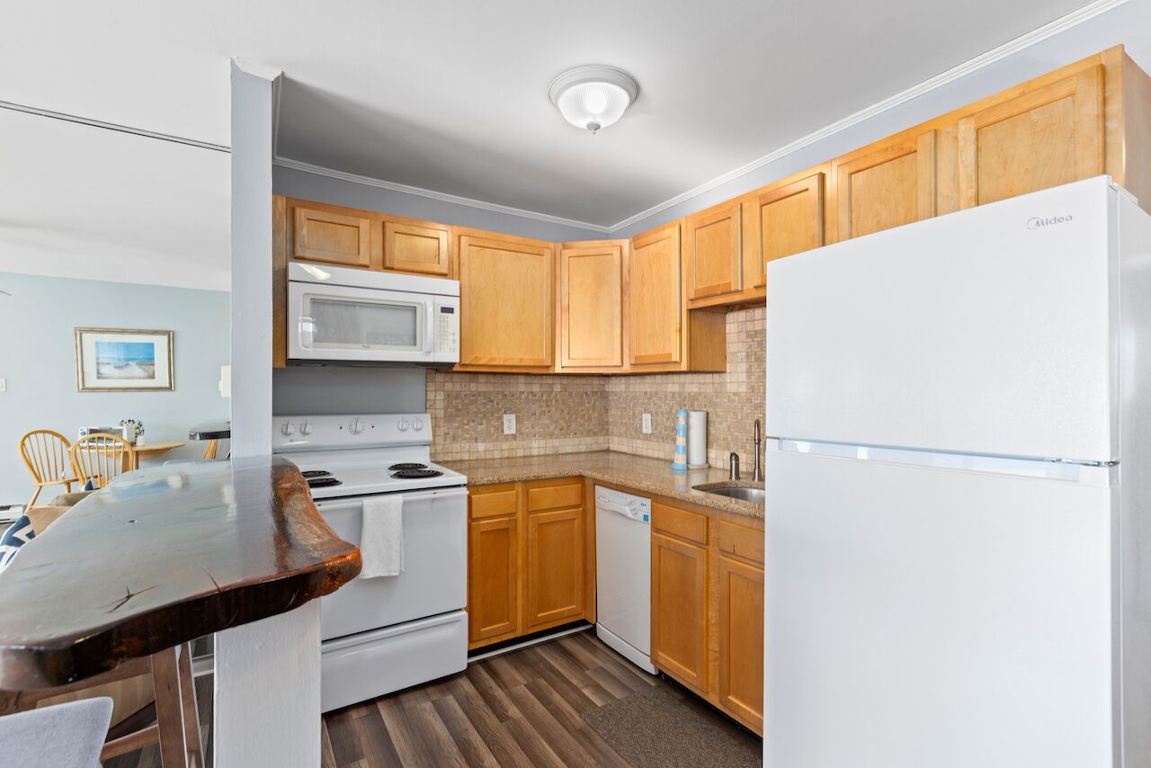 A compact kitchen with wooden cabinets, a white refrigerator, a microwave, a dishwasher, and a stove.