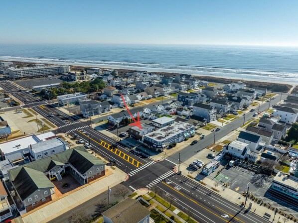 An aerial view of a coastal town with a mix of residential and commercial buildings, a main road, and a beach in the background.