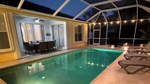 Une piscine dotée d’un patio couvert, comprenant une table et des chaises, ainsi qu’une guirlande lumineuse.