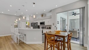 Une cuisine moderne avec des meubles blancs, un îlot central et un coin repas doté de chaises en bois.