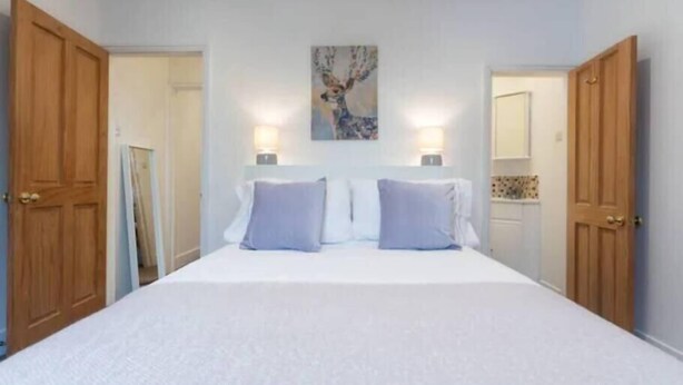 A bedroom with a large bed, two bedside lamps, and a painting on the wall. - Charming Period Home near Surbiton with Garden (Greater London)