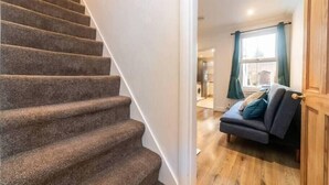 A carpeted staircase leading to a room with a wooden floor, a dark blue sofa, and a window with curtains. - Charming Period Home near Surbiton with Garden (Greater London)