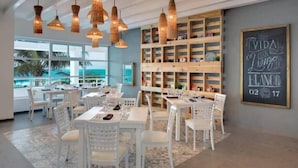 A modern dining area with white furniture and wicker pendant lights. There is a large window with a view of the ocean. - New Studio at the beach, gym, pool, spa. (Cancún)