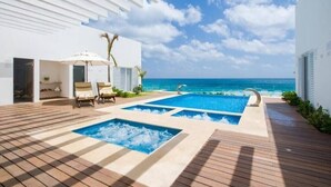 A modern outdoor pool area with a view of the ocean, wooden deck, and lounge chairs. - New Studio at the beach, gym, pool, spa. (Cancún)