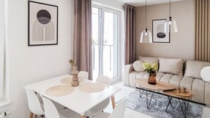 A modern living room with a white dining table, white chairs, a beige sofa, and a coffee table. There are two pendant lights above the sofa and a framed artwork on the wall. - 2 bedroom gorgeous apartment in Biskupiec (Biskupiec)