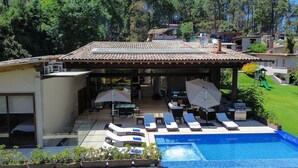 Una casa moderna con piscina, mobiliario exterior y un patio cubierto.