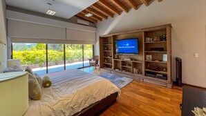 Un dormitorio con una cama grande, un televisor montado en un estante de madera y vistas al exterior.