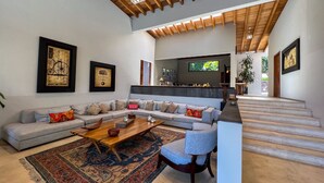 Amplia sala de estar con un sofá grande, una mesa de centro y un televisor. Se ve una escalera que sube a otro nivel.