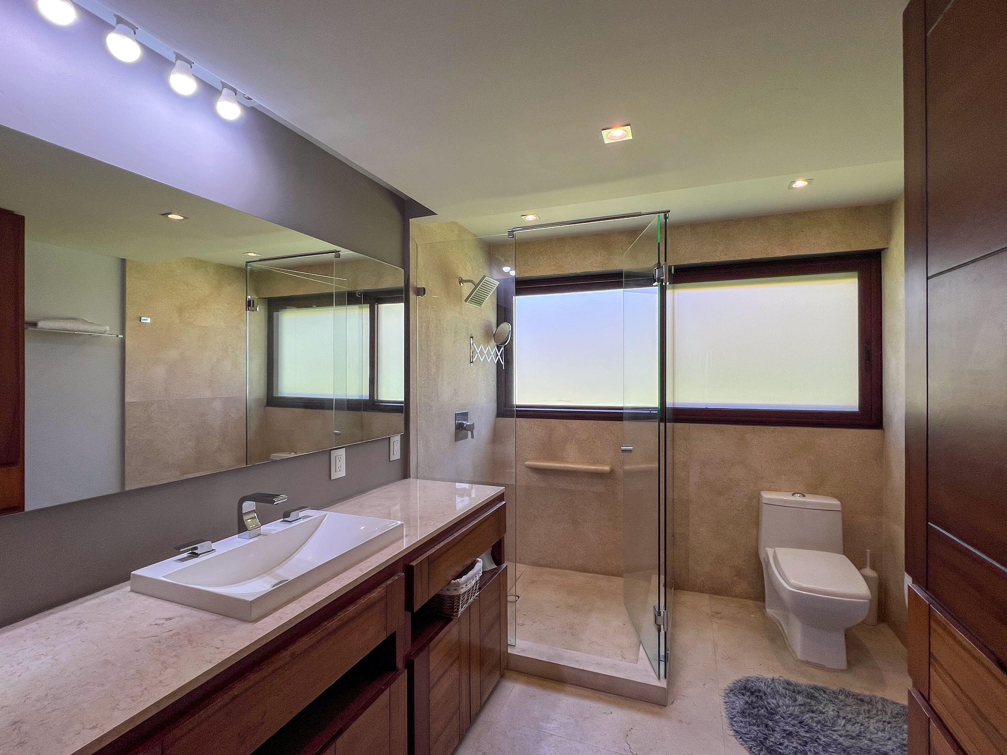 Un baño moderno con un espejo grande, un lavamanos, cabina de ducha y un inodoro.