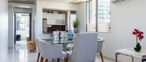 A modern kitchen with a glass dining table, grey upholstered chairs, and a marble countertop.