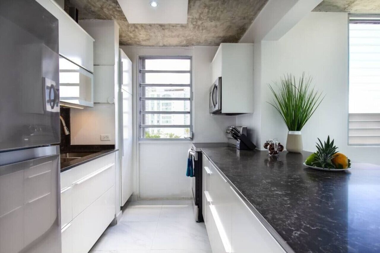 Una cocina moderna con armarios blancos, encimera negra y ventana que deja entrar luz natural.