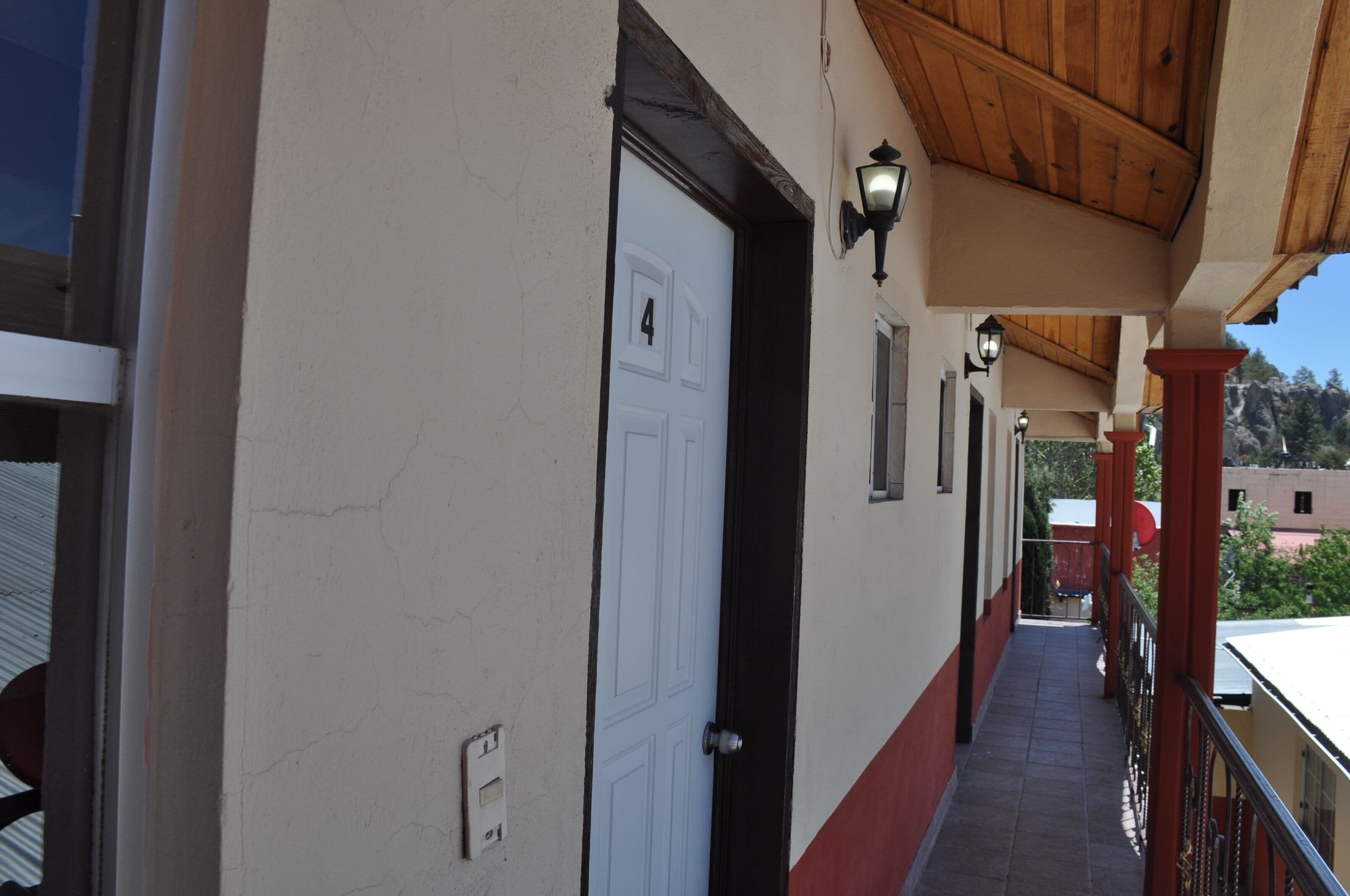 A corridor with a white door, a wooden ceiling, and a red railing.