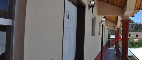 A corridor with a white door, a wooden ceiling, and a red railing.