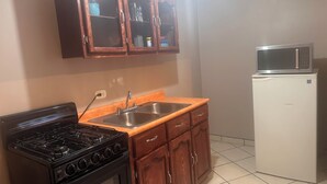Una cocina compacta con estufa a gas, armarios de madera, un lavamanos y un refrigerador blanco.