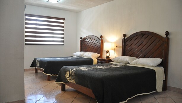 Una habitación con dos camas de madera, una mesita de noche con lámpara y una ventana con persianas.