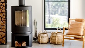 A modern living room with a black wood-burning stove, wicker baskets, and a wicker chair with cushions. - Forever Sunday - Plunge Pool, Woodfire pizza oven, Outdoor firepit (Little Forest)