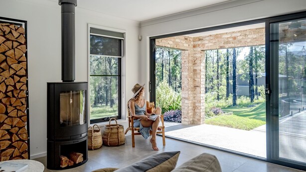 A modern living room with a fireplace, large windows, and a view of a garden. - Forever Sunday - Plunge Pool, Woodfire pizza oven, Outdoor firepit (Little Forest)