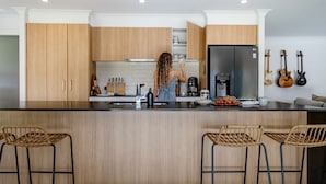 A modern kitchen with wooden cabinets, a stainless steel refrigerator, and a bar area with wicker chairs. - Forever Sunday - Plunge Pool, Woodfire pizza oven, Outdoor firepit (Little Forest)