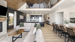 A modern living room with a sectional sofa, dining area, kitchen, and a balcony. - Lakeview Cabin w/ Hot Tub, Pool, Decks - Sleeps 20 (Branson)