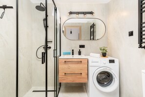 Une salle de bain moderne avec une douche à parois de verre, un lavabo intégré avec un miroir, un meuble-lavabo en bois et un lave-linge à chargement frontal.