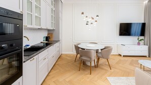 Une cuisine moderne avec des meubles blancs, un four encastré et un coin repas comprenant une table ronde et des chaises.