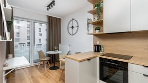 A modern kitchen with a built-in oven, a dining area with a round table and chairs, and a large window with a view of the city. - Walerego Sławka Cosy Studio (Kraków)