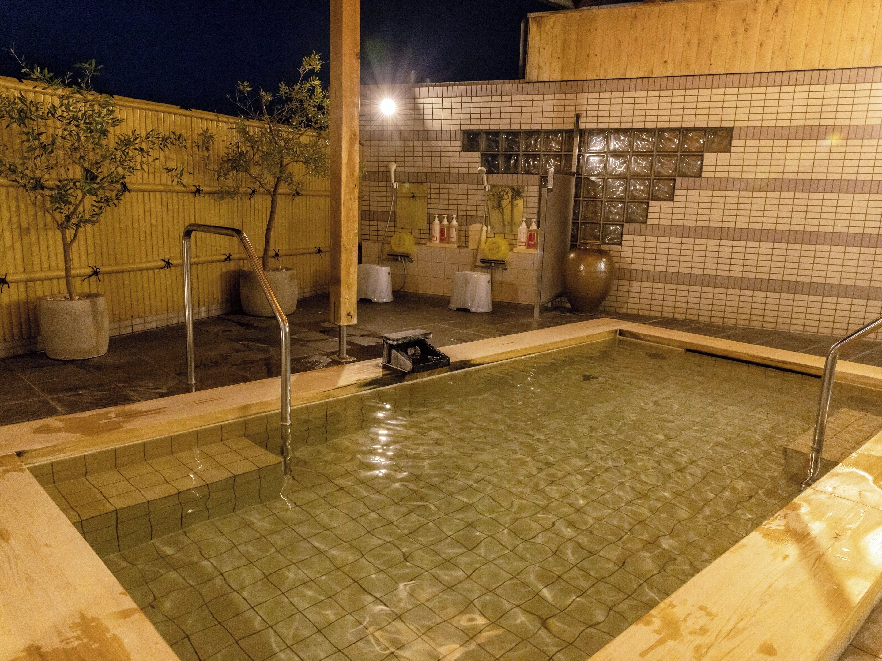 A rectangular outdoor pool with a tiled floor, surrounded by a wooden fence and potted plants.