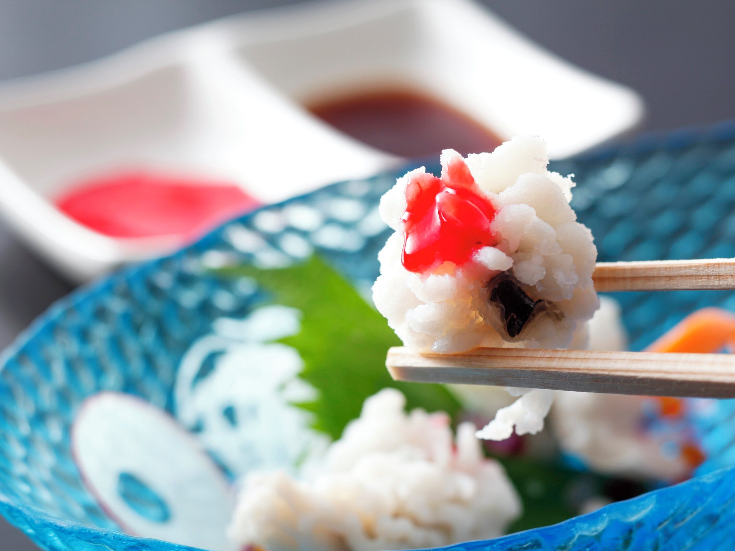 Un primo piano di riso per sushi con un pezzo di pesce e un condimento rosso su un bastoncino di legno.