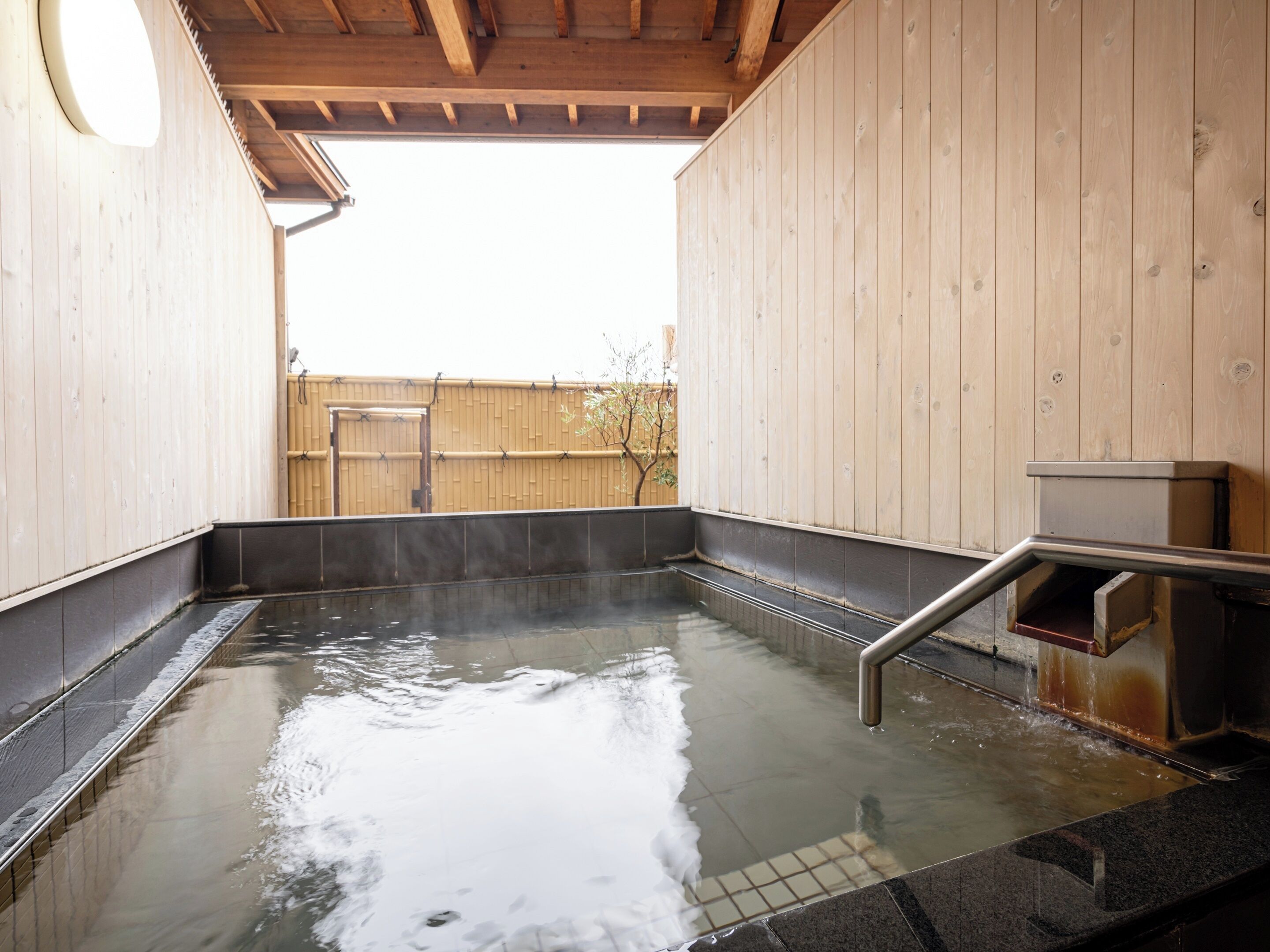A hot spring bath area with wooden walls, a tiled floor, and a metal bench.