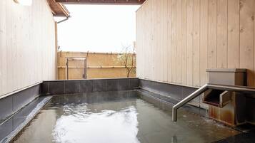 A hot spring bath area with wooden walls, a tiled floor, and a metal bench.