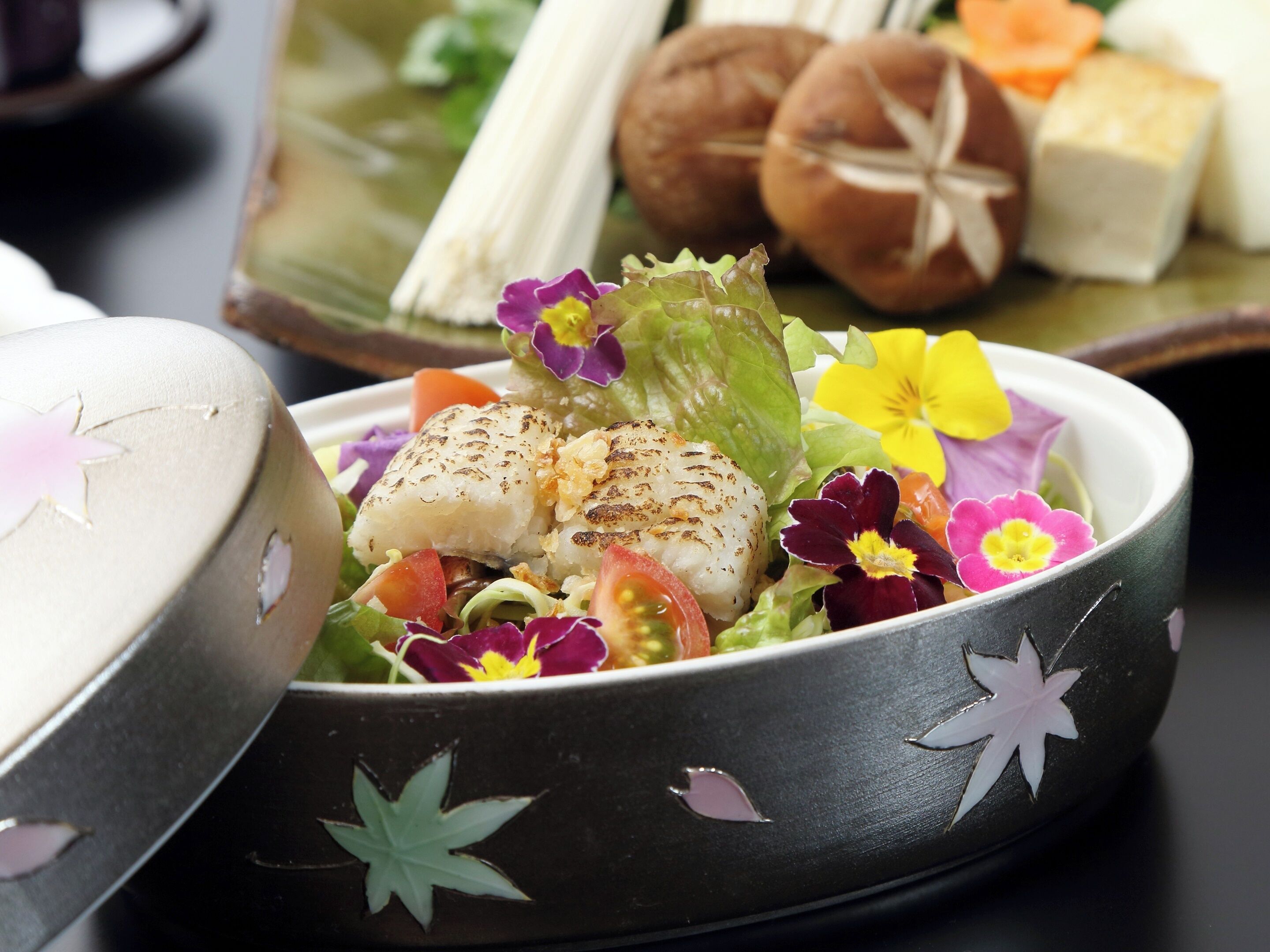 A bowl of food with grilled fish, vegetables, and flowers.