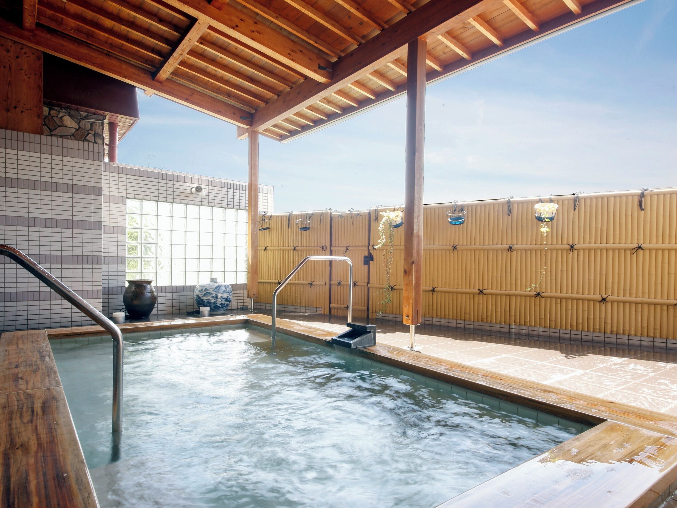 A hot tub area with a wooden deck, tiled walls, and a bamboo fence.