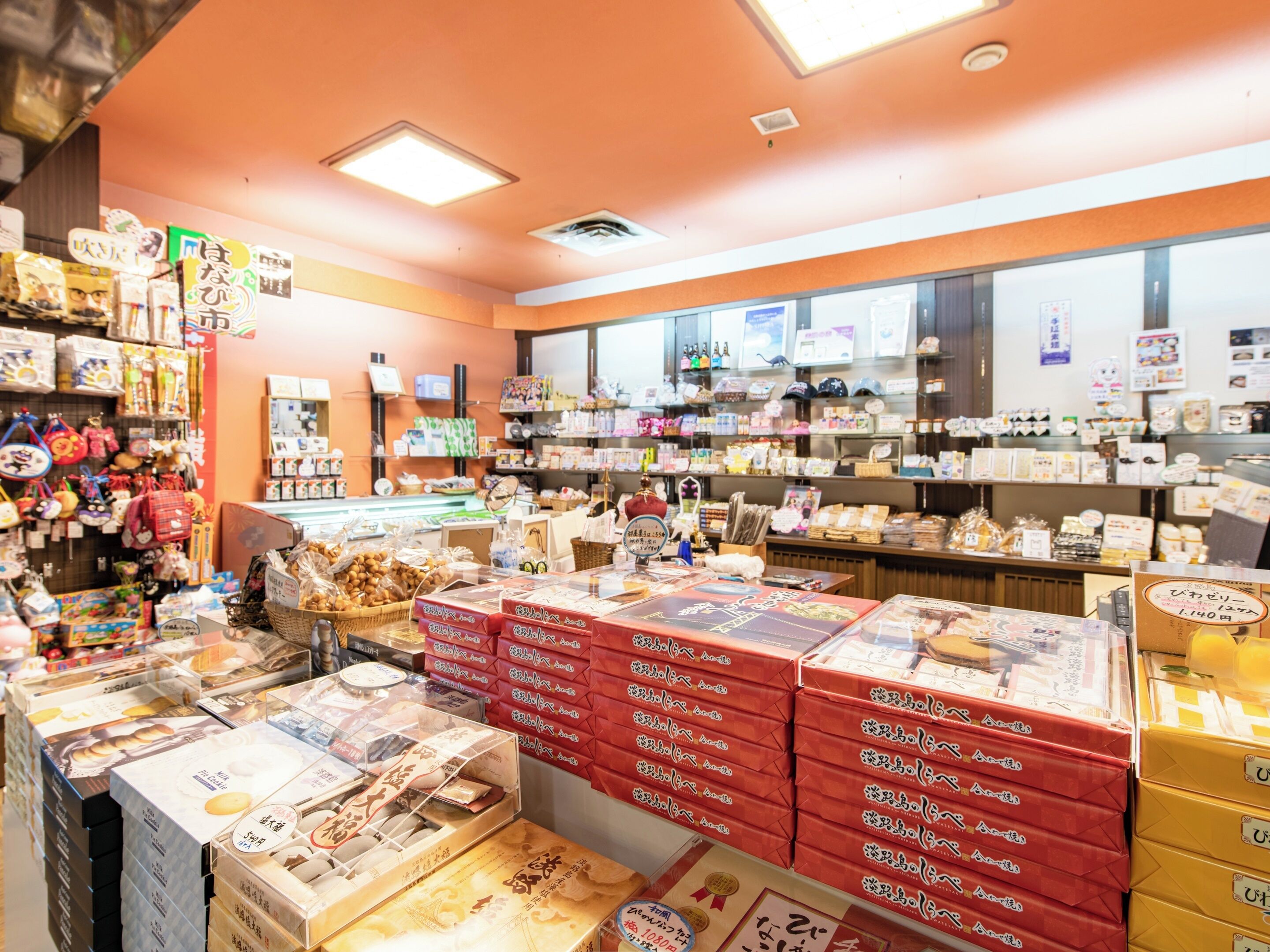 A store interior with shelves stocked with various products, a display counter with boxed items, and a ceiling with fluorescent lights.