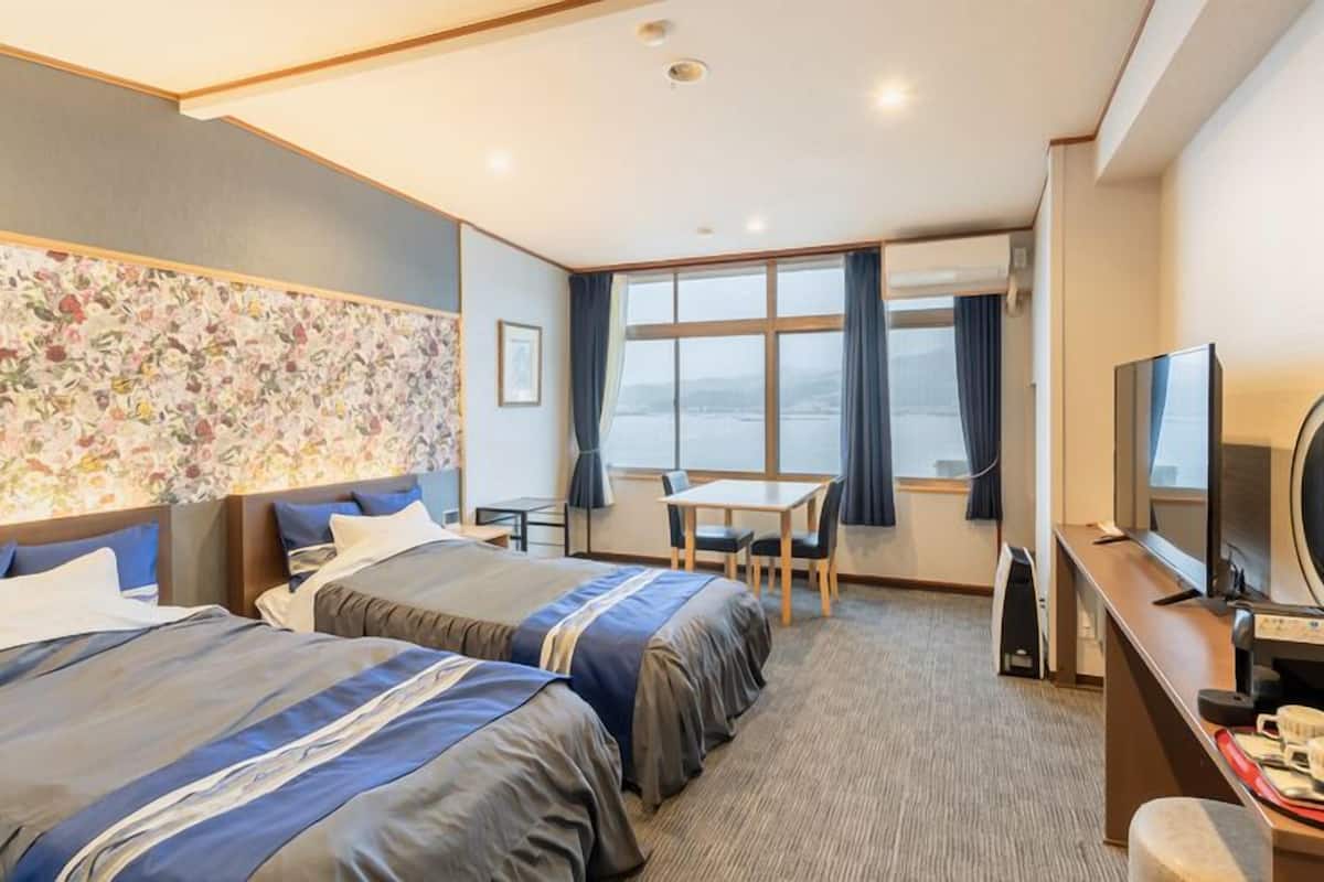 Habitación de hotel con dos camas, un escritorio, un televisor y un ventanal grande.