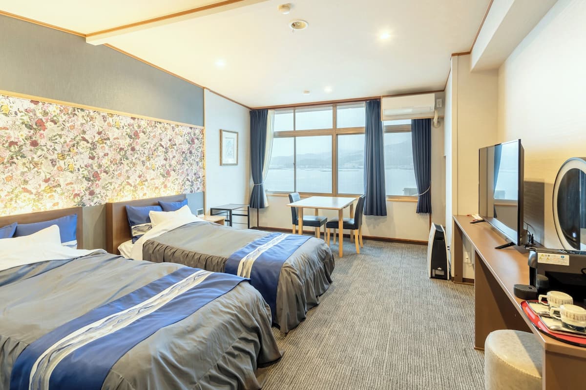 Ein Hotelzimmer mit zwei Betten, einem Schreibtisch, einem Fernseher und Blick aufs Meer.