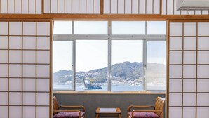 A traditional Japanese room with tatami flooring, a shoji screen, and a view of a harbor with mountains in the background. - Shiozaki Onsen Awajishima kaijyo Hotel (Minamiawaji)