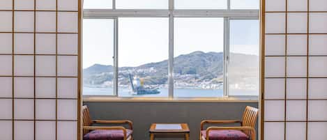 A traditional Japanese room with tatami flooring, a shoji screen, and a view of a harbor with mountains in the background.