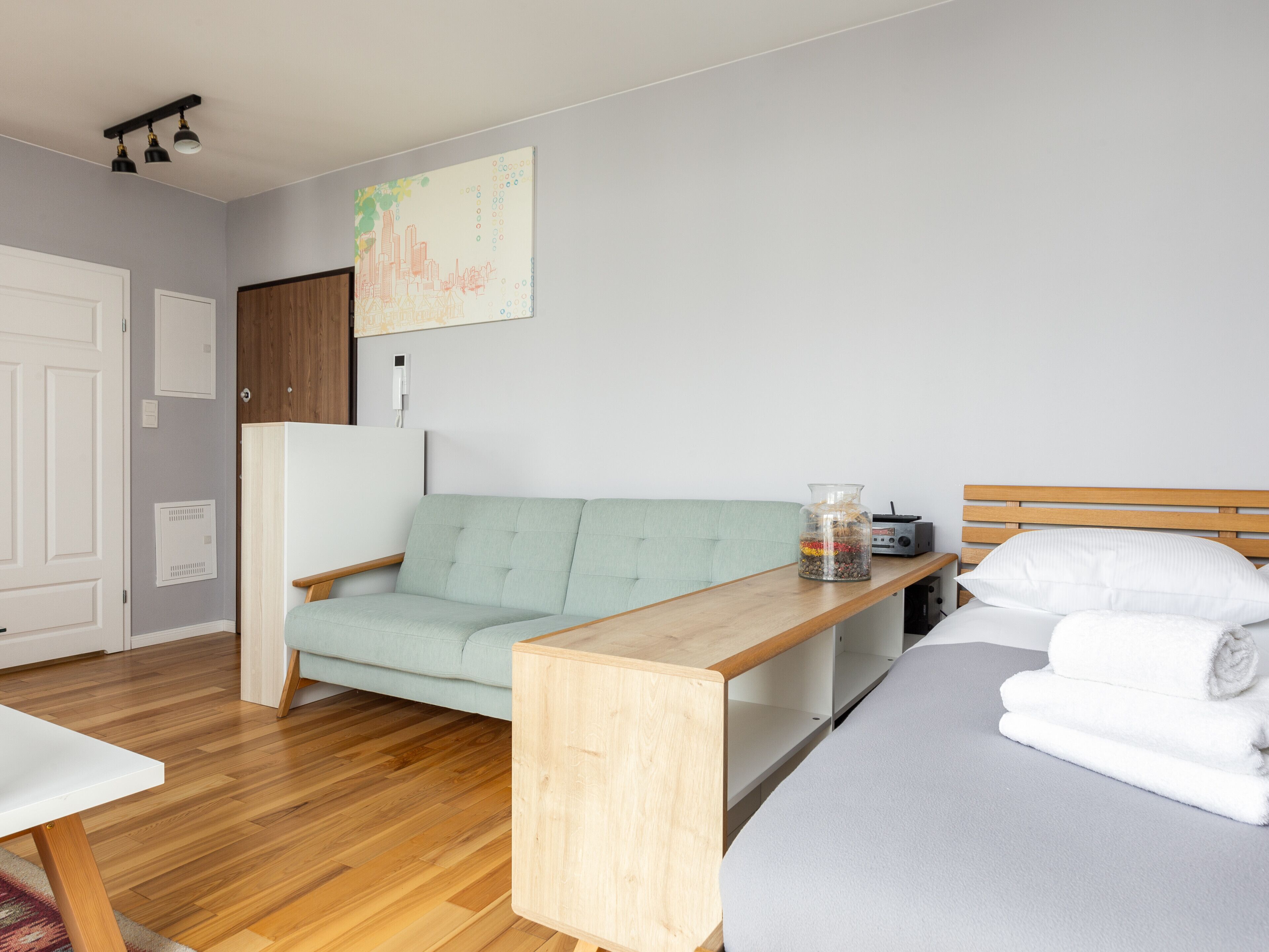 Een moderne slaapkamer met een lichtgroene bank, een houten nachtkastje, een bed met witte beddengoed en een radio bevestigd aan de muur.