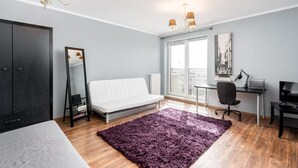 A modern bedroom with a bed, a desk, a chair, a large mirror, and a view of the city through the window.