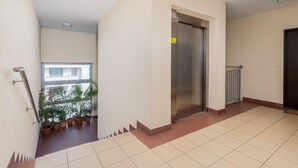 A clean, modern hallway with a tiled floor, a door leading to a room, and potted plants along the wall.