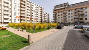 A residential building with multiple balconies, a paved walkway, and parked cars.