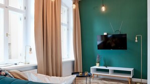 Uma sala de estar moderna com um sofá verde-água, uma TV de tela plana na parede e piso de madeira em padrão herringbone.