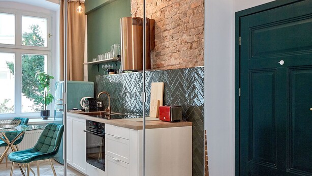 Uma cozinha moderna com parede de tijolos, uma janela grande e uma porta verde.