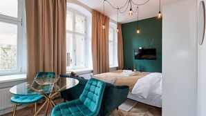 Quarto de hotel moderno com cama, cadeiras verde-água, mesa de vidro e parede verde decorativa.