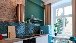 Cozinha moderna com parede de tijolos, geladeira azul e mesa de vidro com cadeiras.