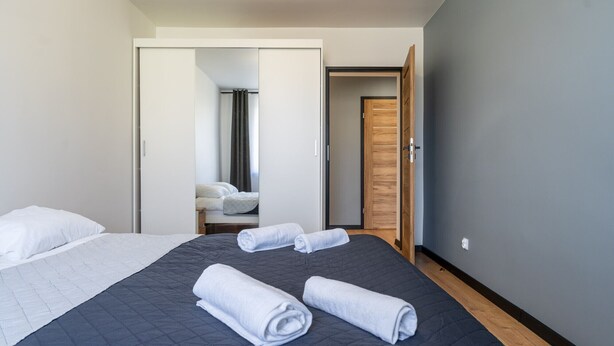 Une chambre d’hôtel moderne avec un grand lit, deux serviettes roulées, une armoire en bois et une porte donnant accès à la salle de bain.
