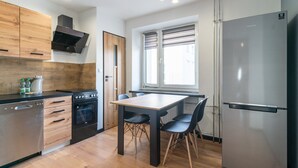 Une cuisine moderne avec des meubles en bois, un réfrigérateur en acier inoxydable, un four encastré et une table à manger avec des chaises.